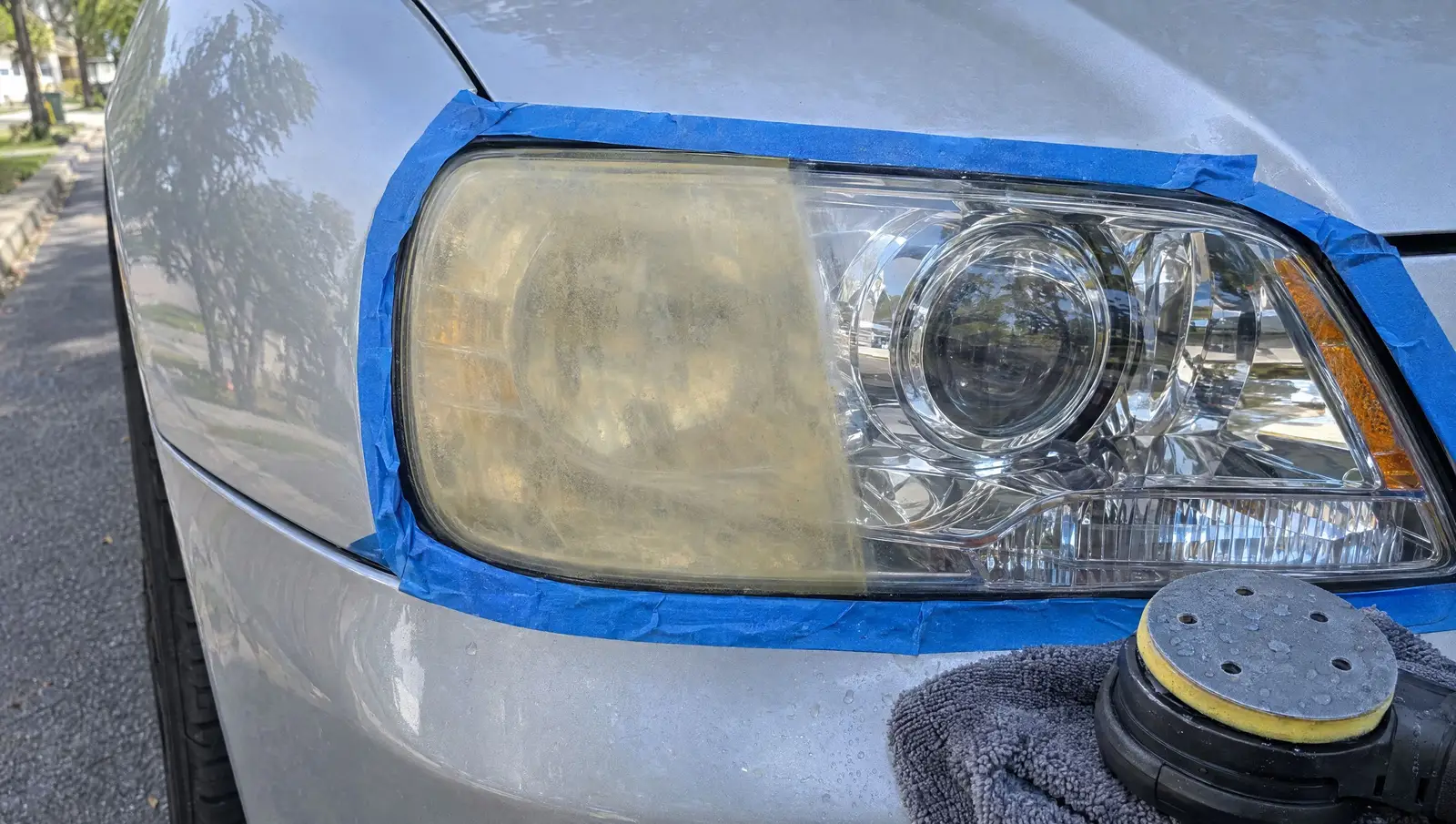 Headlight taped off, left half still yellow and hazy, right half polished clear, polisher on the bumper