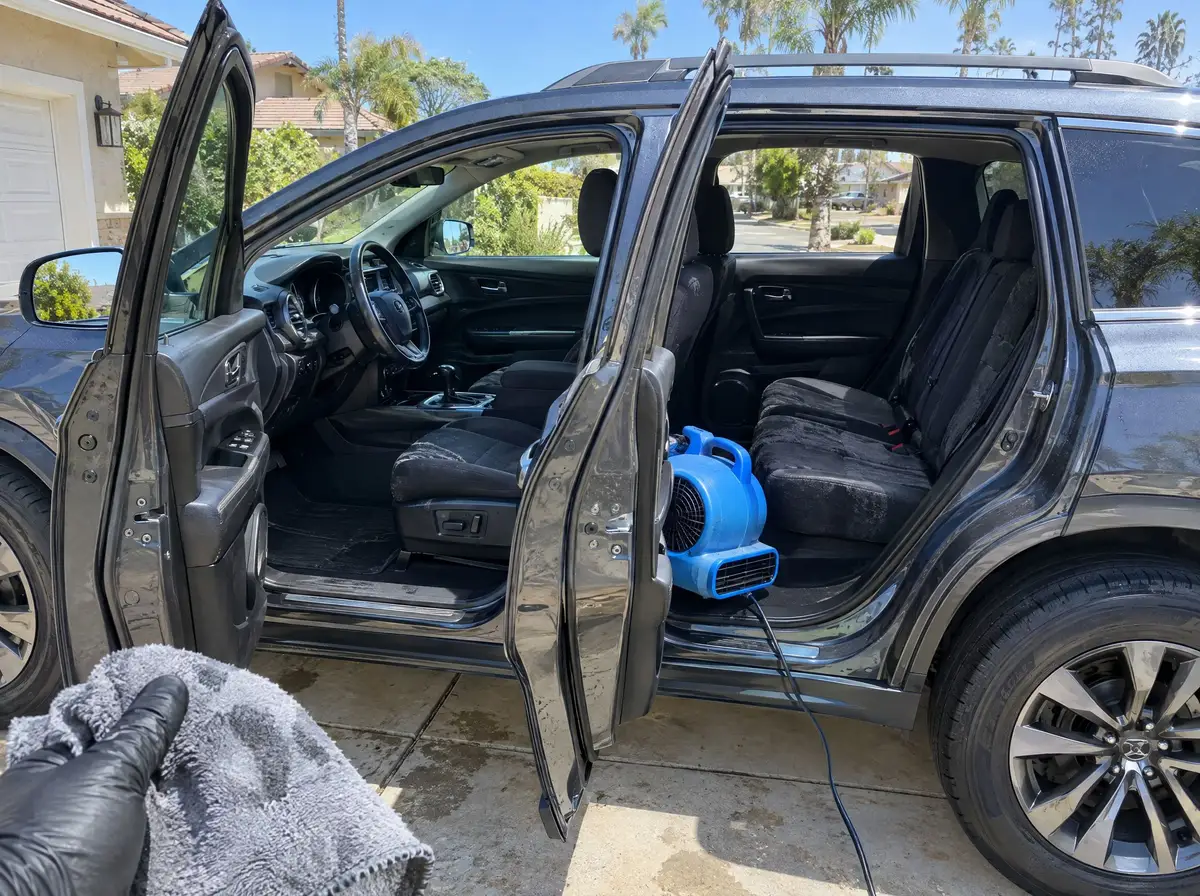 SUV with all doors open in a sunny driveway, an air mover blowing into the back seat to dry it