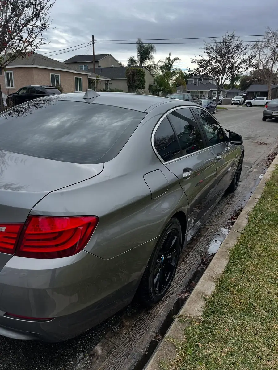 Rear of a grey BMW 528i after a detail, the street wet beside it