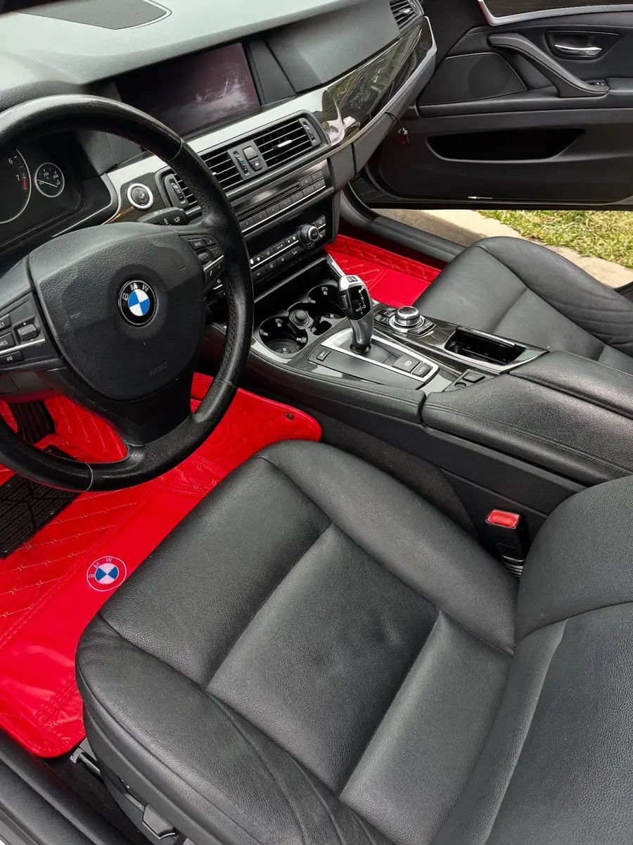 Cleaned front interior of a BMW with black leather seats and red floor mats