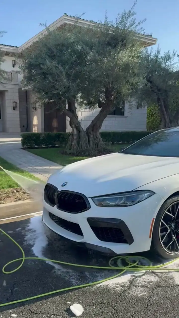 White BMW M8 being rinsed in a driveway during a mobile wash
