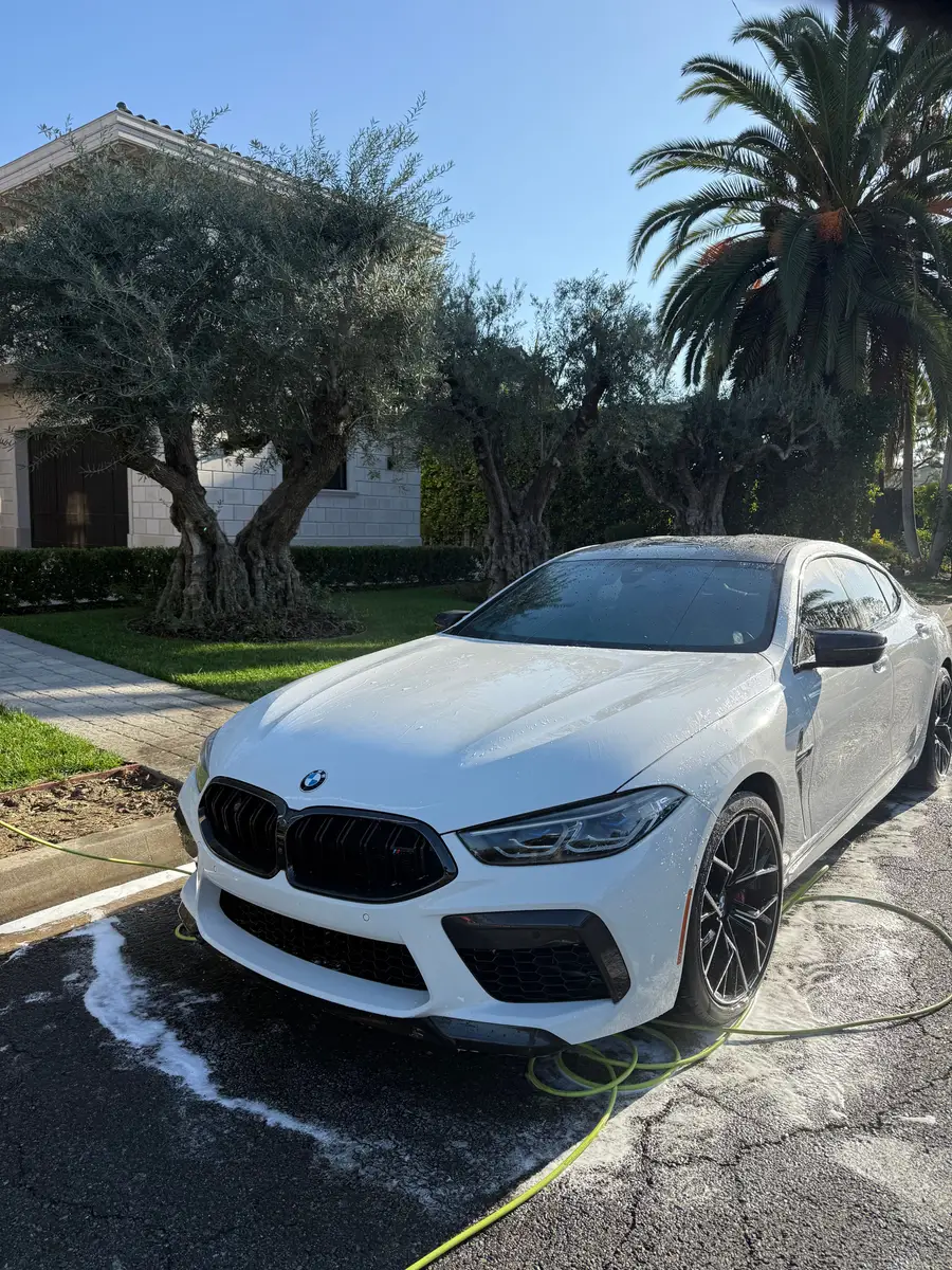 White BMW M8 in a driveway during a wash, hose on the wet pavement
