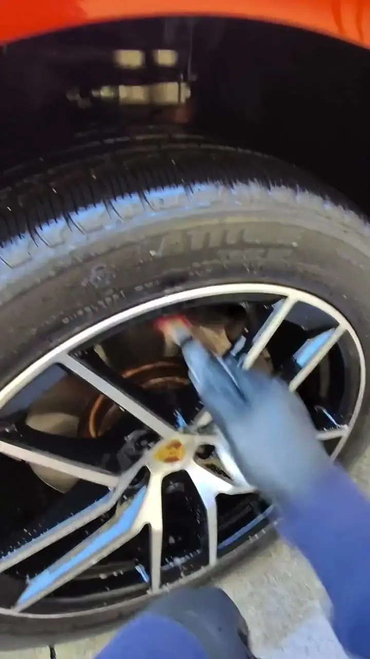 Wheel brush cleaning the spokes of an orange Porsche Macan