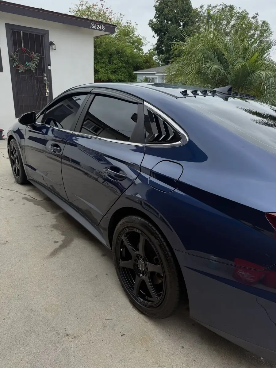 Side of a navy Hyundai Sonata after a detail, the paint reflecting the house