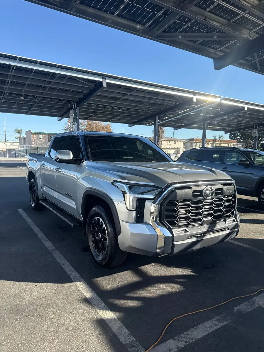 Silver Toyota Tundra under a solar carport in a parking lot, a hose on the wet pavement beside it